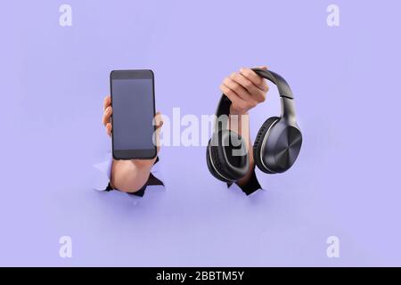 Le smartphone et le casque bluetooth se tiennent sur un fond bleu déchiré. Espace de copie. Concept d'application Music Mobile. Banque D'Images