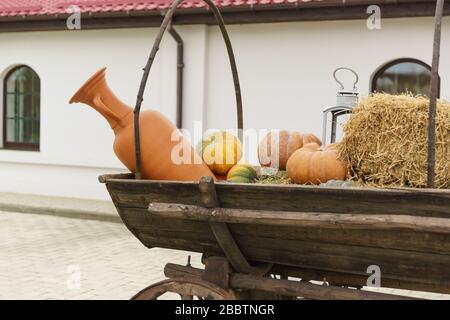 Pichet en terre cuite et citrouilles orange sur un chariot en bois. Cour de ferme Banque D'Images