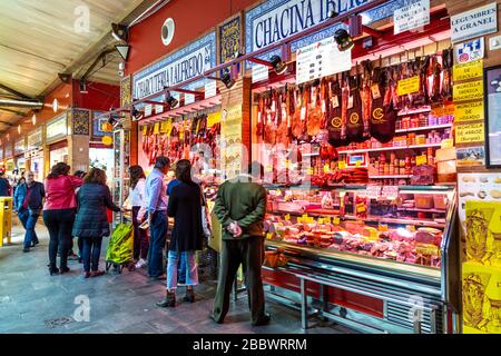 Les gens font du shopping dans un boucherie et un comptoir déli au marché de Triana (Mercado de Triana), Séville, Andalousie, Espagne Banque D'Images