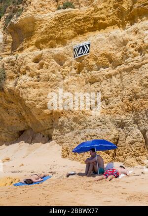 Les gens qui bronzer sous un signe de danger pour la rockfall, côte ouest d'Alporchinhas, Algarve, Portugal Banque D'Images