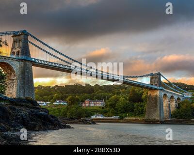 Lever du soleil au pont suspendu Menai reliant l'île d'Anglesey au Pays de Galles du continent, conçu par Thomas Telford et ouvert en 1826 Banque D'Images