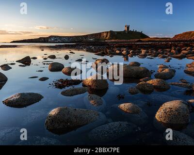 Les ruines du château de Dunstanburgh surplombant les rives de rochers parsemées de la baie d'Embleton, Northumberland, Angleterre Banque D'Images