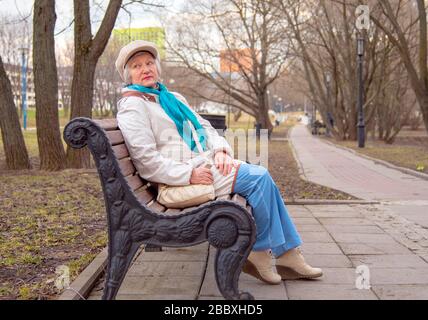 Une vieille femme habillée avec élégance est assise sur un banc dans une ruelle. Banque D'Images