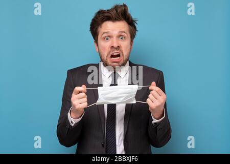 Un jeune homme beau avec masque médical a une attaque de panique. Il a peur qu'il soit infecté. Studio tourné sur un mur bleu Banque D'Images