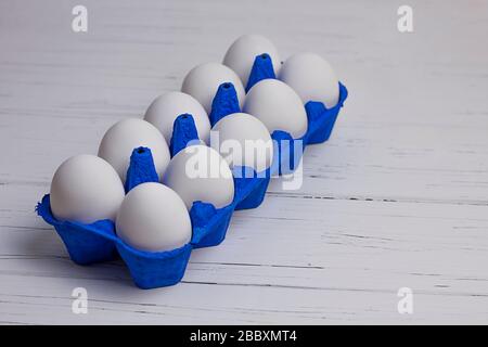 dix œufs blancs en uniforme bleu sur fond clair en bois Banque D'Images
