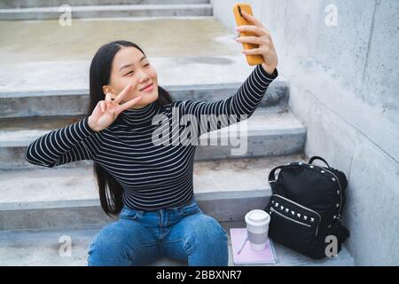 Portrait de jeune femme tenant une belle asiatique avec des selfies son téléphone portable tout en étant assis sur des escaliers à l'extérieur. Banque D'Images