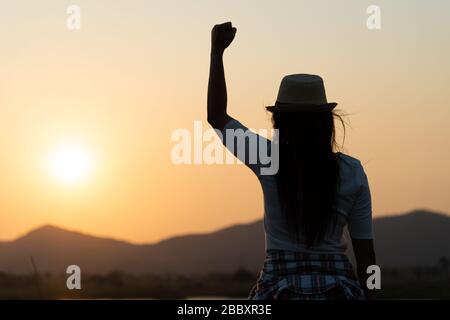 Femme avec poing dans l'air pendant le coucher du soleil lever montagne en arrière-plan. Tenez-vous fort. Sentiment motivé, liberté, force et courage concept. Banque D'Images