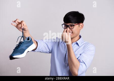 Gros plan homme asiatique tenant la chaussure sale et laiteuse avec une expression de dégoût. Concept de santé. Banque D'Images