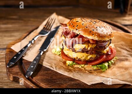 Hamburger américain juteux, hamburger ou cheeseburger avec deux viandes de bœuf, sauce et sur fond noir. Concept de restauration rapide américaine Banque D'Images