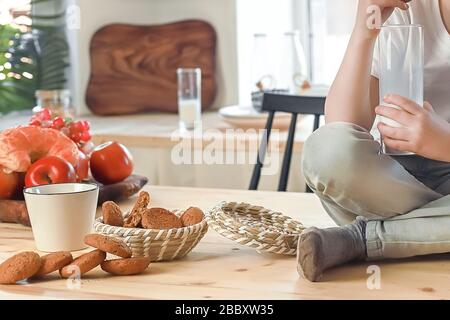 Petit garçon caucasien assis sur la table de la cuisine et manger des biscuits au gruau avec du lait. Petit déjeuner sain avant l'école et la maternelle à la maison. Banque D'Images