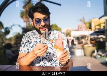 Portrait de jeune homme profitant du beau temps tout en mangeant une glace à l'extérieur. Banque D'Images