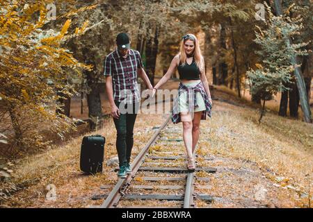 Un jeune couple d'amoureux a manqué le train. Marcher sur les rails dans la forêt d'automne en attendant le prochain train. Banque D'Images