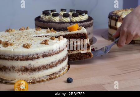 Les mains de la femme attrapent une tranche de gâteau avec du chocolat blanc sur fond de table en bois. Assortiment de gâteaux de fête. Banque D'Images