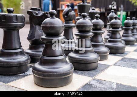 Gros plan sur des pièces d'échecs noires de taille humaine avec des pions devant Banque D'Images