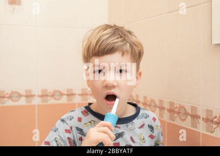 un petit garçon blond en pyjama brosse ses dents le matin avant le petit déjeuner. Banque D'Images