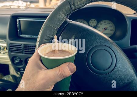 vue sur un verre de cacao, de chocolat, de boisson chaude à la main des conducteurs derrière la roue d'une voiture Banque D'Images