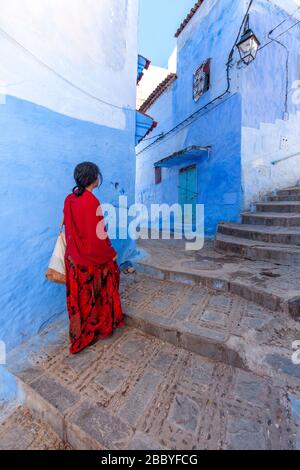 Chefchaouen, Maroc : une femme en rouge marchant dans la Médina Banque D'Images