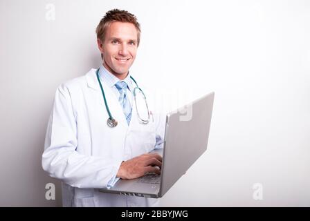 Un médecin sympathique dans un blouse de laboratoire blanc et un stéthoscope souriant tenant son ordinateur portable Banque D'Images