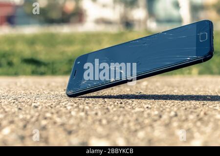 Gros plan d'un smartphone moderne qui tombe sur l'écran d'asphalte et de craquage. Téléphone portable cassé avec des fissures sur l'écran et l'espace de copie. Banque D'Images