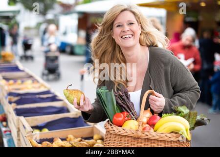 Une femme d'âge moyen avec un sourire positif fait du shopping sur un marché hebdomadaire Banque D'Images