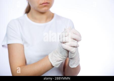 Fille paramédic met des gants médicaux blancs sur les mains. Protection contre les germes et les virus. Elle est dans un T-shirt blanc sur un fond blanc. Banque D'Images