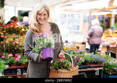 Une jolie femme d'âge moyen achète heureusement des fleurs sur un marché Banque D'Images