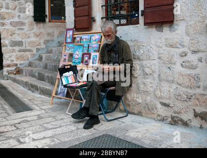 Monténégro, 17 septembre 2018 : un artiste se trouve à côté de ses peintures exposées dans la rue de la vieille ville de Kotor Banque D'Images