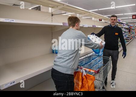 Membre du personnel du supermarché qui remet aux clients un paquet de rouleaux de toilettes par personne lors de l'achat pandémique de Coronavirus au Royaume-Uni, mars 2020 Banque D'Images