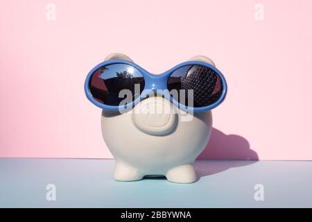 Porc moneybox blanc avec lunettes de soleil sur fond rose et bleu Banque D'Images