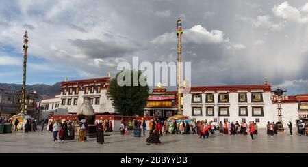 Temple de Jokhang sous un ciel nuageux. Vue panoramique sur le patrimoine mondial de l'UNESCO avec roue dorée Dharma. Pèlerins en premier plan. Banque D'Images