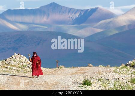 Paysage du plateau tibétain avec chaîne de montagnes. Au premier plan, une femelle, pèlerin bouddhiste avec une roue de prière à la main. Vêtu d'un peignoir rouge. Banque D'Images