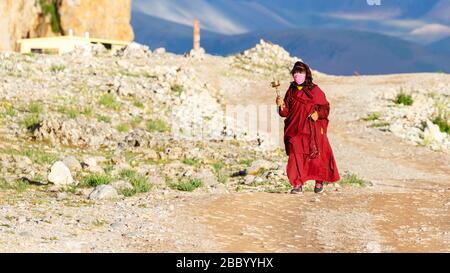 Pèlerin féminin marchant sur le Kora. Oscillation d'une roue de prière manuelle. Dans le fond montains du plateau tibétain avec ciel et nuages. Bouddhisme tibétain Banque D'Images