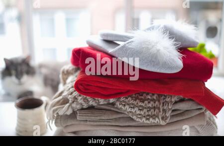 pile de sweaters tricotés confortables et de pantoufles hom. près de la grande fenêtre. En arrière-plan, un chat flou n'est plus concentré. PET et vêtements chauds. Concept automne-hiver. Espace de copie. Banque D'Images