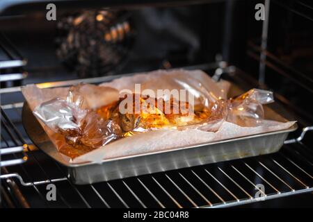 Le porc est cuit dans un manchon sur une plaque de cuisson en métal dans le four. Banque D'Images