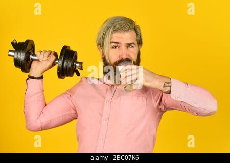 Exercice dans la salle de sport. Lait bons nutriments. Quantité de graisse. Vitamines pour les muscles. Le sportif tient un haltère et un verre de lait. Régime protéique. Cocktail de protéines. Source de calcium. L'homme barbu boit du lait. Banque D'Images