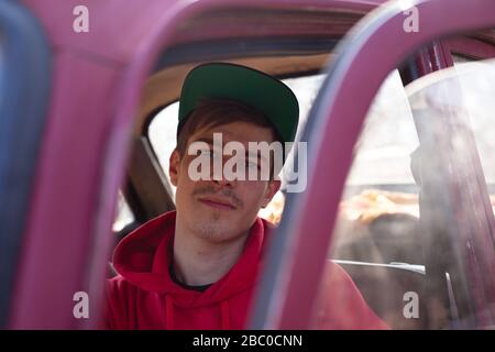 l'homme est assis sur le siège du conducteur d'une voiture rouge, en regardant par une porte ouverte. conducteur fatigué après un long voyage. Banque D'Images