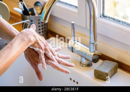 Vue rapprochée sur les mains d'une femme se lavant soigneusement les mains avec du savon sous le robinet de l'évier de cuisine. Banque D'Images