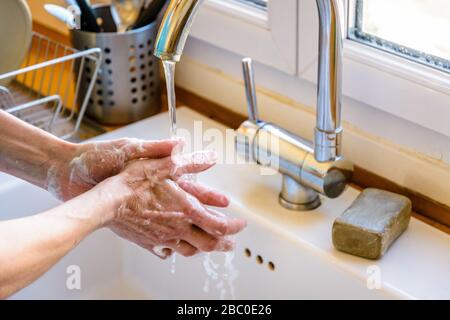 Vue rapprochée sur les mains d'une femme se lavant soigneusement les mains avec du savon sous le robinet de l'évier de cuisine. Banque D'Images