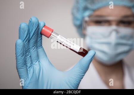 Femme en costume de protection, respirateur et lunettes qui tiennent un tube à essai avec échantillon de résultat positif d'analyse infecté par le coronavirus COVID - 19 2019-n Banque D'Images