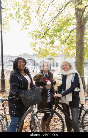 Portrait souriant, confiant actif femmes âgées amis avec café et vélos dans le parc d'automne Banque D'Images
