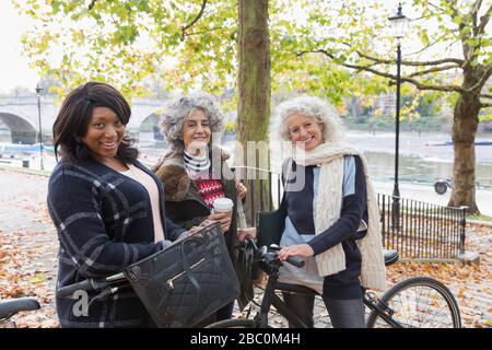 Portrait souriant, confiant actif femmes âgées amis avec café et vélos dans le parc d'automne Banque D'Images