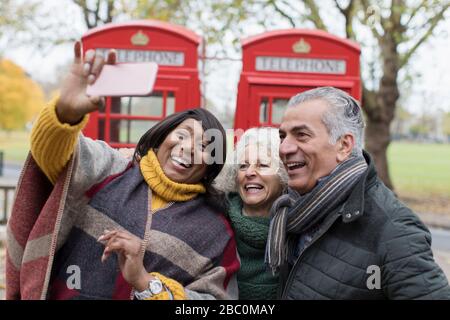 Des amis seniors prenant le selfie devant les cabines téléphoniques rouges dans le parc d'automne Banque D'Images