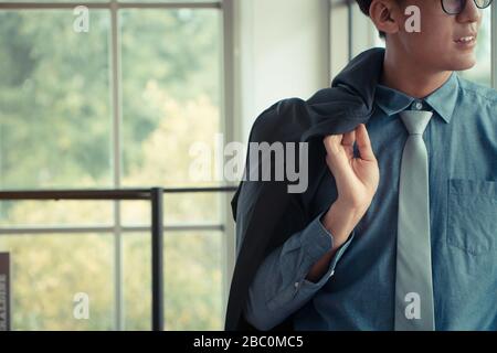 Portrait d'un jeune homme d'affaires heureux et souriant debout à côté des fenêtres et tenant son costume. Concept de jeunes entrepreneurs qui sont fiers des affaires Banque D'Images