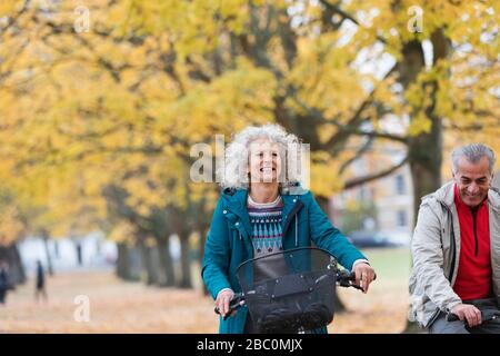 Femme senior souriante et insouciante qui fait du vélo parmi les arbres dans le parc d'automne Banque D'Images