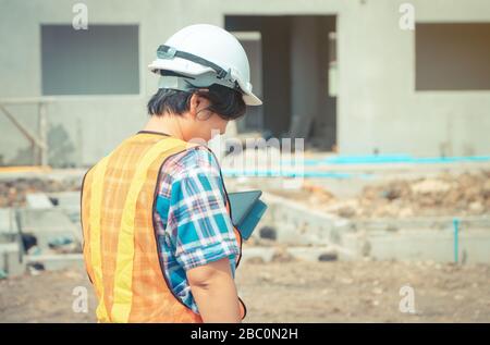 Les femmes asiatiques engineering est titulaire d'une tablette pour une utilisation dans l'inspection des chantiers de construction pour plus de précision et en conformité avec le plan. Concept de l'égalité de Banque D'Images