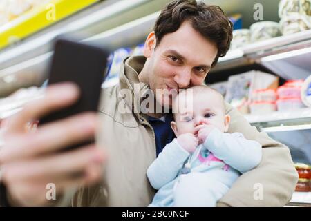 Père affectueux et fille de bébé prenant selfie dans le supermarché Banque D'Images