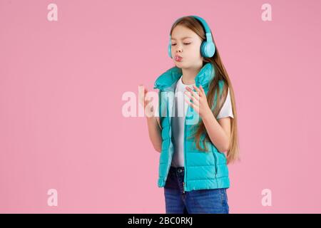 Une petite fille avec casque explose la gomme à mâcher rose sur un fond rose. Banque D'Images