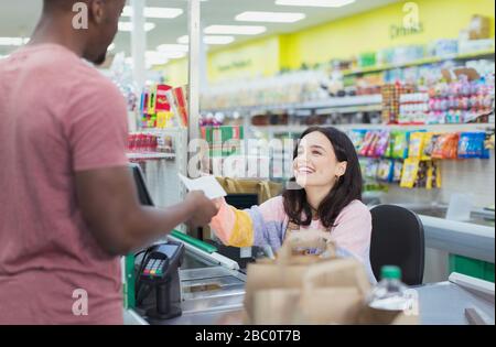 Caissier souriant donnant un reçu au client au moment du contrôle du supermarché Banque D'Images