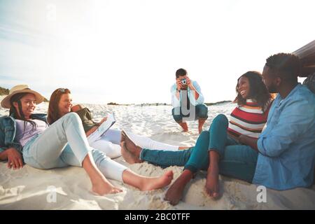 Jeune homme avec appareil photo numérique photographier des amis se détendre sur la plage Banque D'Images