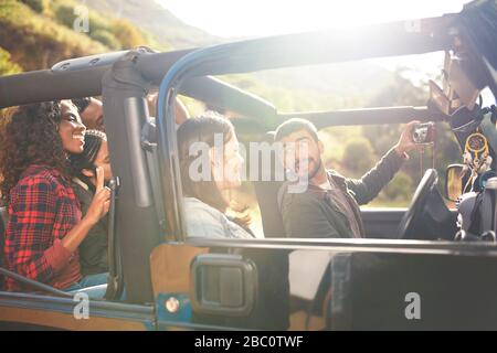 Homme avec appareil photo numérique prenant selfie en jeep avec des amis Banque D'Images